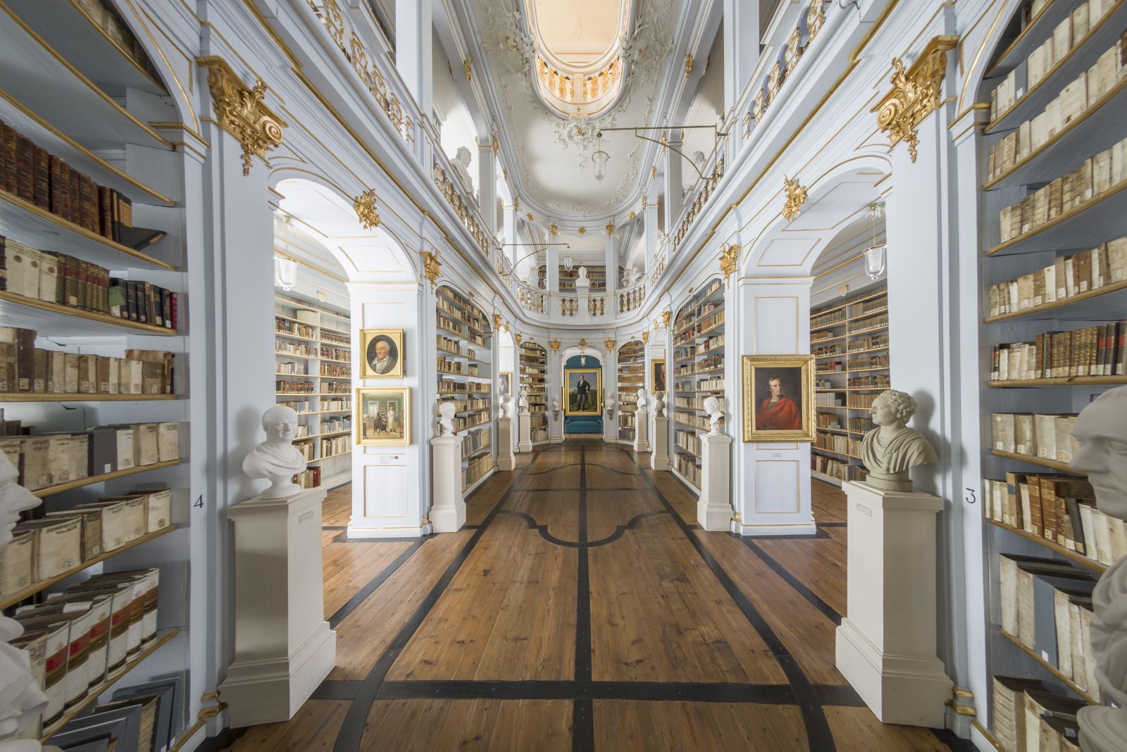 Zentraler Blick ins Oval des Rokokosaals, weiß-goldene Bücherregale mit historischen Büchern links und rechts