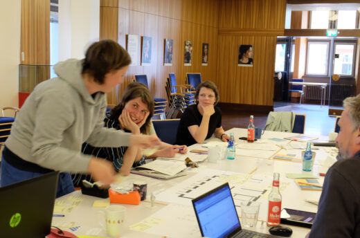 Das Foto zeigt mehrere Personen an einem Tisch sitzend, die sich gemeinsam in einer Workshopsituation befinden.
