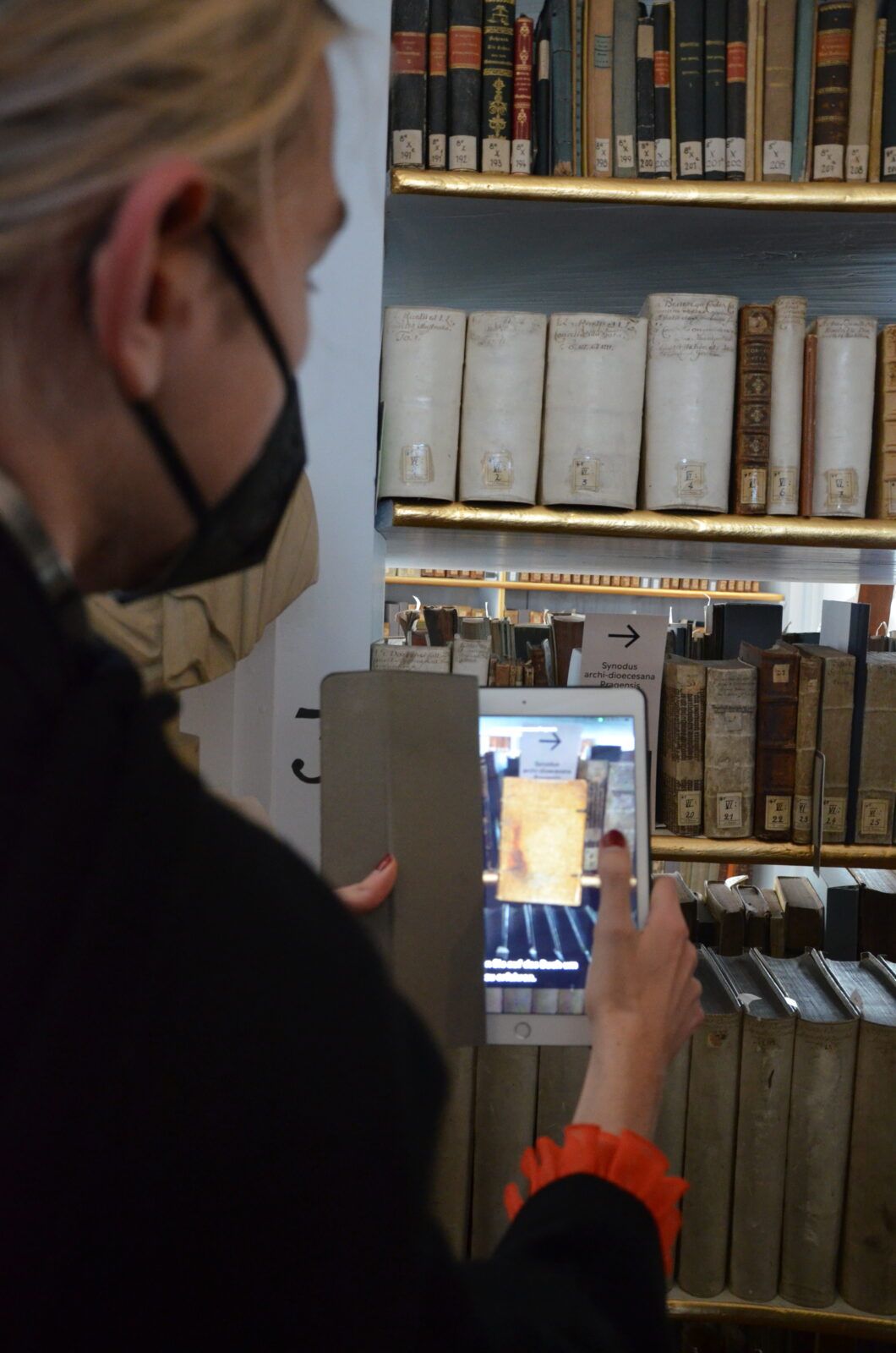 Frau in Rückansicht vor Bücherregal mit 3D-Buch auf Tablet-Screen