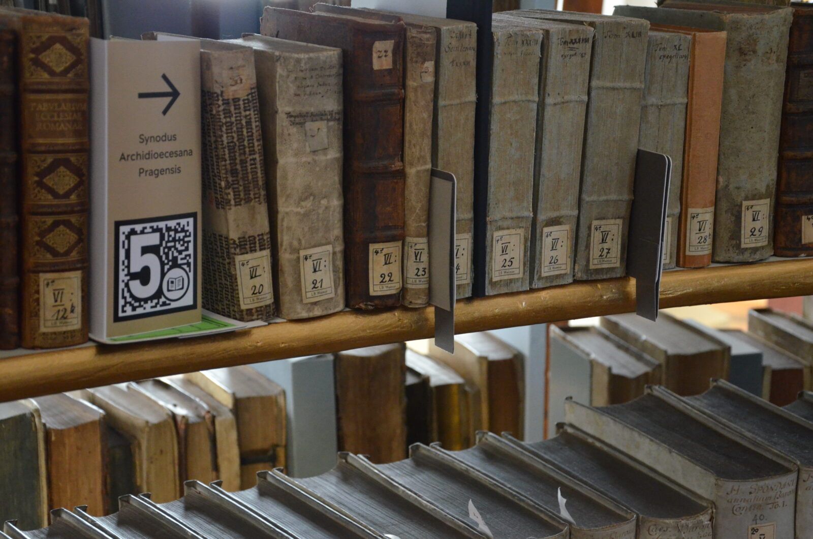 Bücherregal, in dem sich zwischen den historischen Büchern ein beigefarbenes Label mit AR-Marker, Buchtitel und Pfeil nach rechts befindet