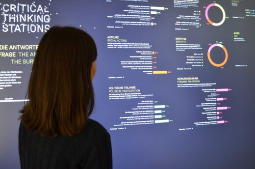 Eine junge Frau steht vor einer Wand der Critical Thinking Station, auf der statistische Auswertungen zu sehen sind