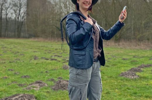 Eine junge Frau steht in Outdoorklamotten und Handy in der Hand im Museumspark Kalkriese.