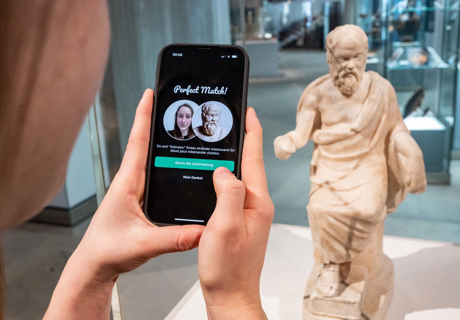 Auf dem Foto ist ein Smartphone abgebildet, dass ein "Match" mit einem Kunstobjekt zeigt. Im Hintergrund ist eben dieses Kunstobjekt zu sehen.