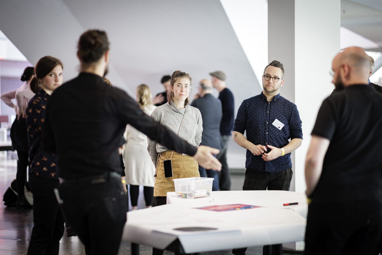 In lockerer Arbeitsatmosphäre stehen mehrere Menschen um einen Tisch, der für ein World-Café Format vorbereitet ist, herum.