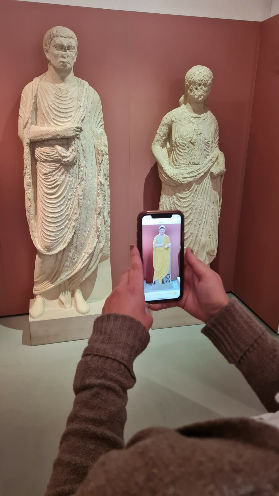 Zu sehen sind Grabfiguren, deren farbliche Darstellung auf dem Smartphone rekonstruiert wird.