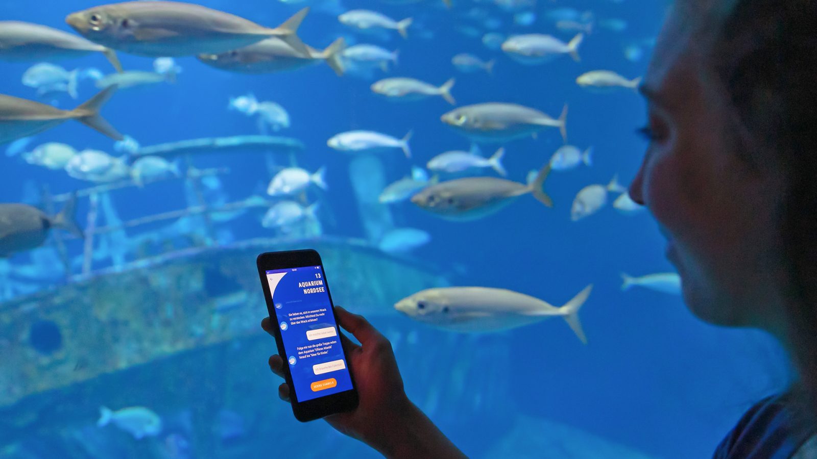 Eine Besucherin nutzt das Smartphone vor einem großen Aquarium.