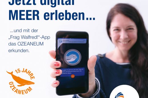 Eine Frau zeigt ihr Smartphone und Texte verkünden Informationen zur App des OZEANEUMs.