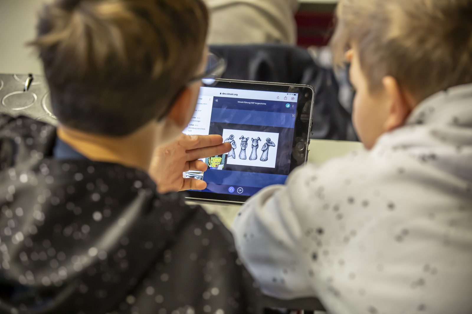 Zwei Schüler sitzen vor einem Tablet. Sie nehmen an einer Vimuki-Führung teil.