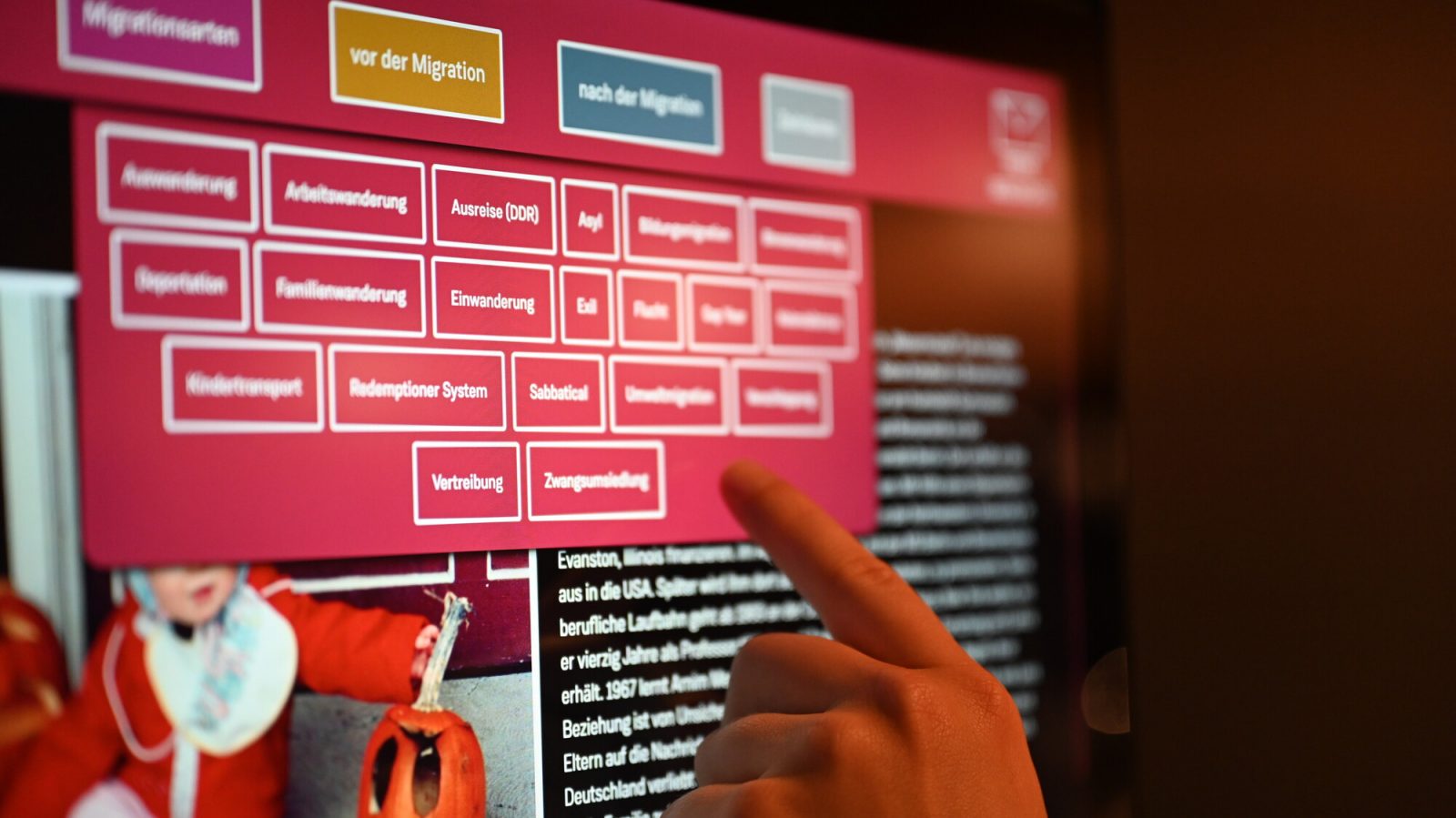 Medienstation mit Auswahlmenü für verschiedene Migrationsgründe. Über einen Touchscreen kann per Berührung mit dem Finger das Gewünschte ausgewählt werden.