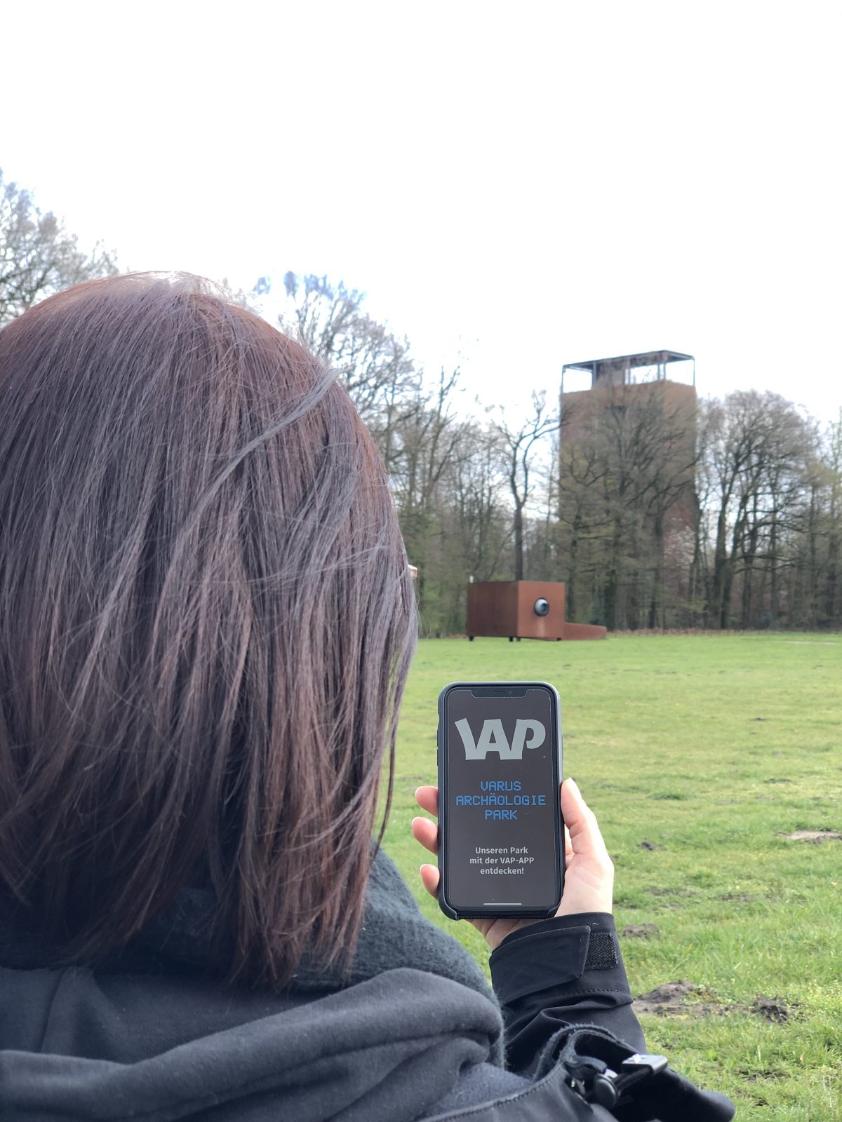 Eine Frau steht mit einem Handy im Museumspark.